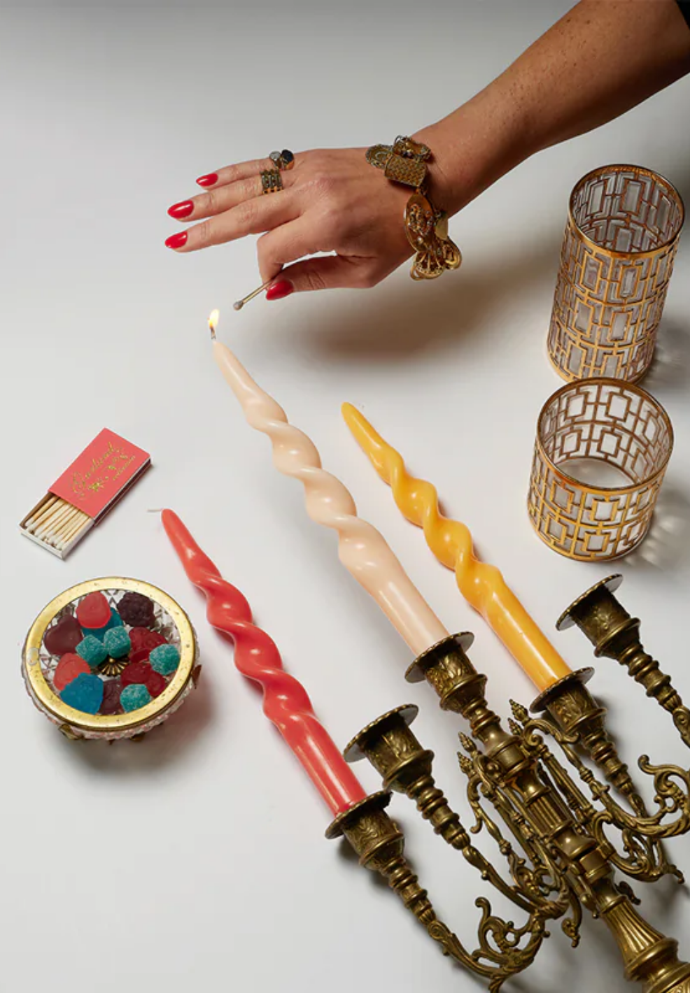 Hand lighting a candle with decorative candles and a candelabra on a white surface.